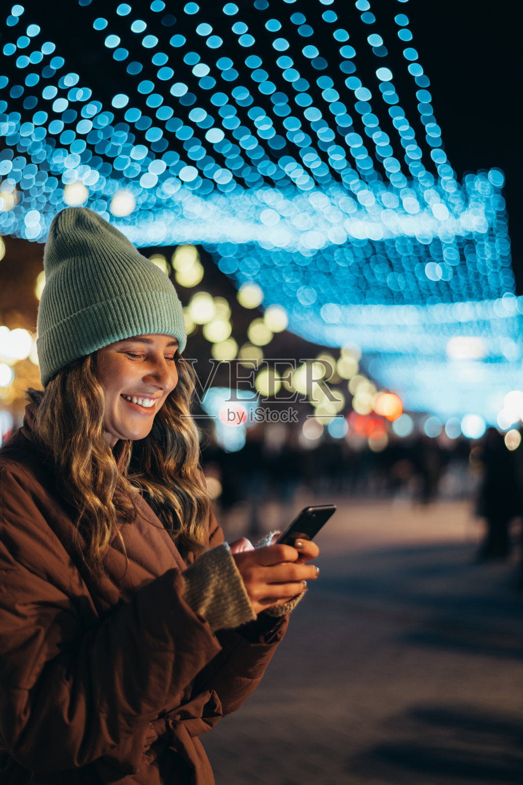 年轻女子在外面用智能手机，背景是圣诞彩灯照片摄影图片
