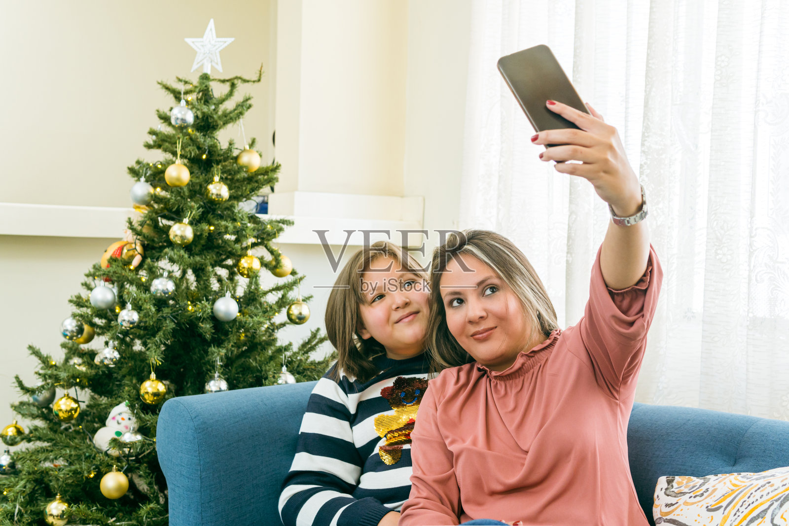 一对母女在圣诞树旁边的客厅里用手机自拍照片摄影图片