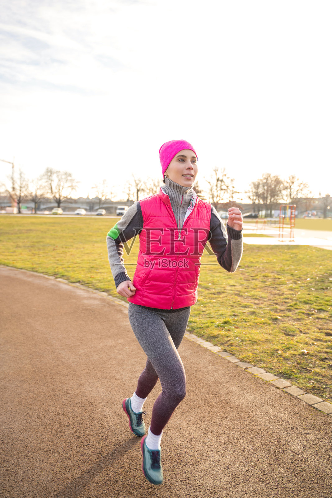 日出时，穿着健身服的年轻白人妇女在运动场上奔跑照片摄影图片