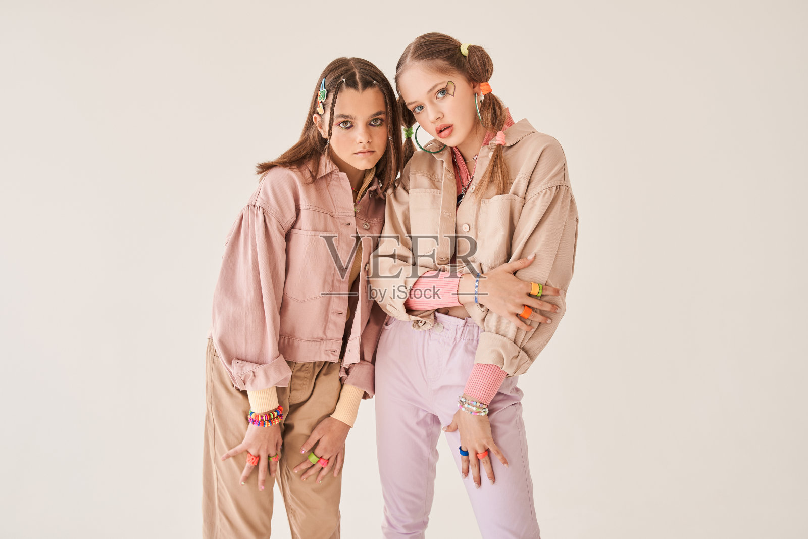 两个闺蜜穿着时髦的衣服在浅米色背景下的工作室摆姿势照片摄影图片