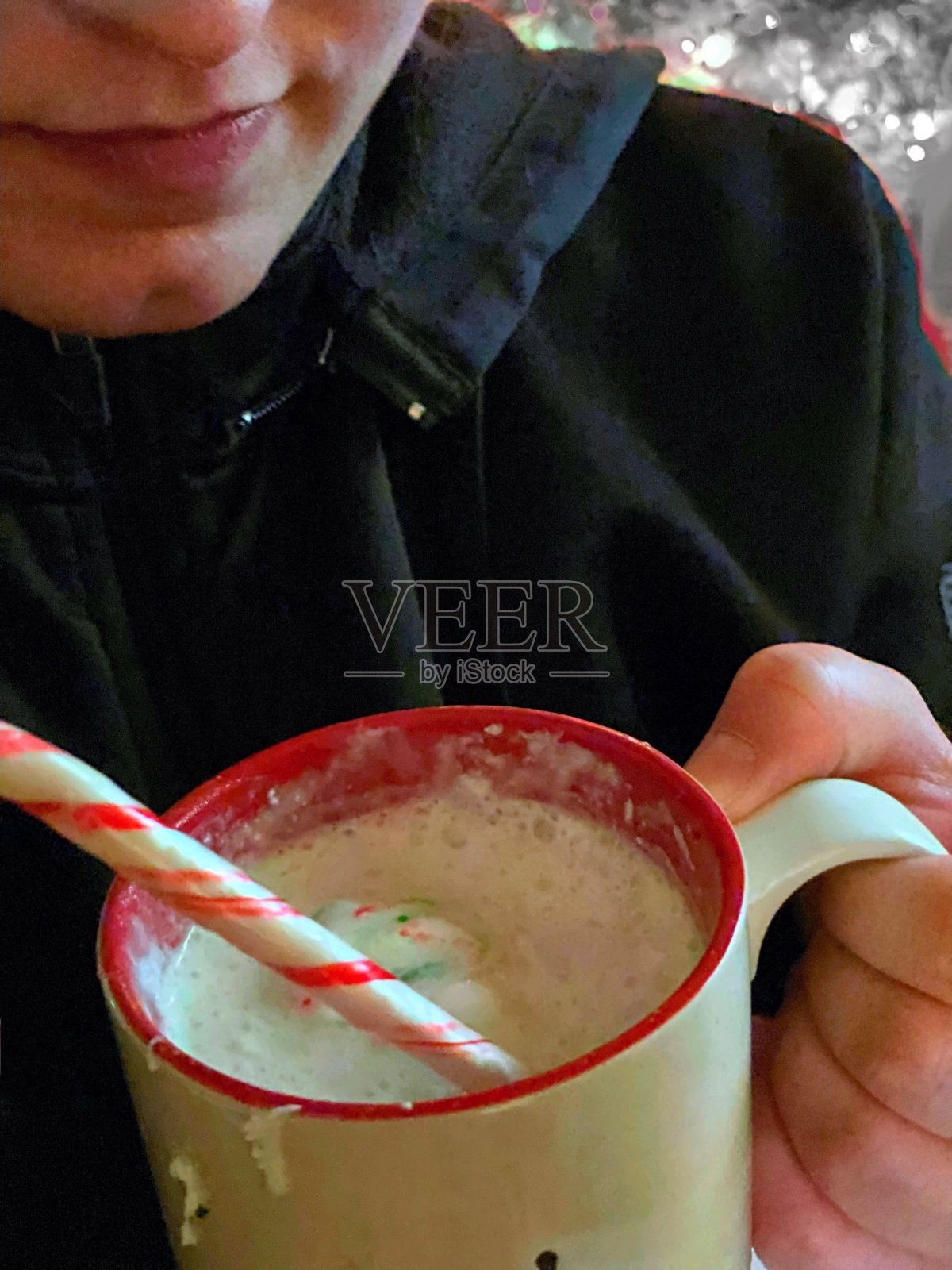 年轻女子用薄荷棒搅拌一杯热可可汤料中的鲜奶油照片摄影图片