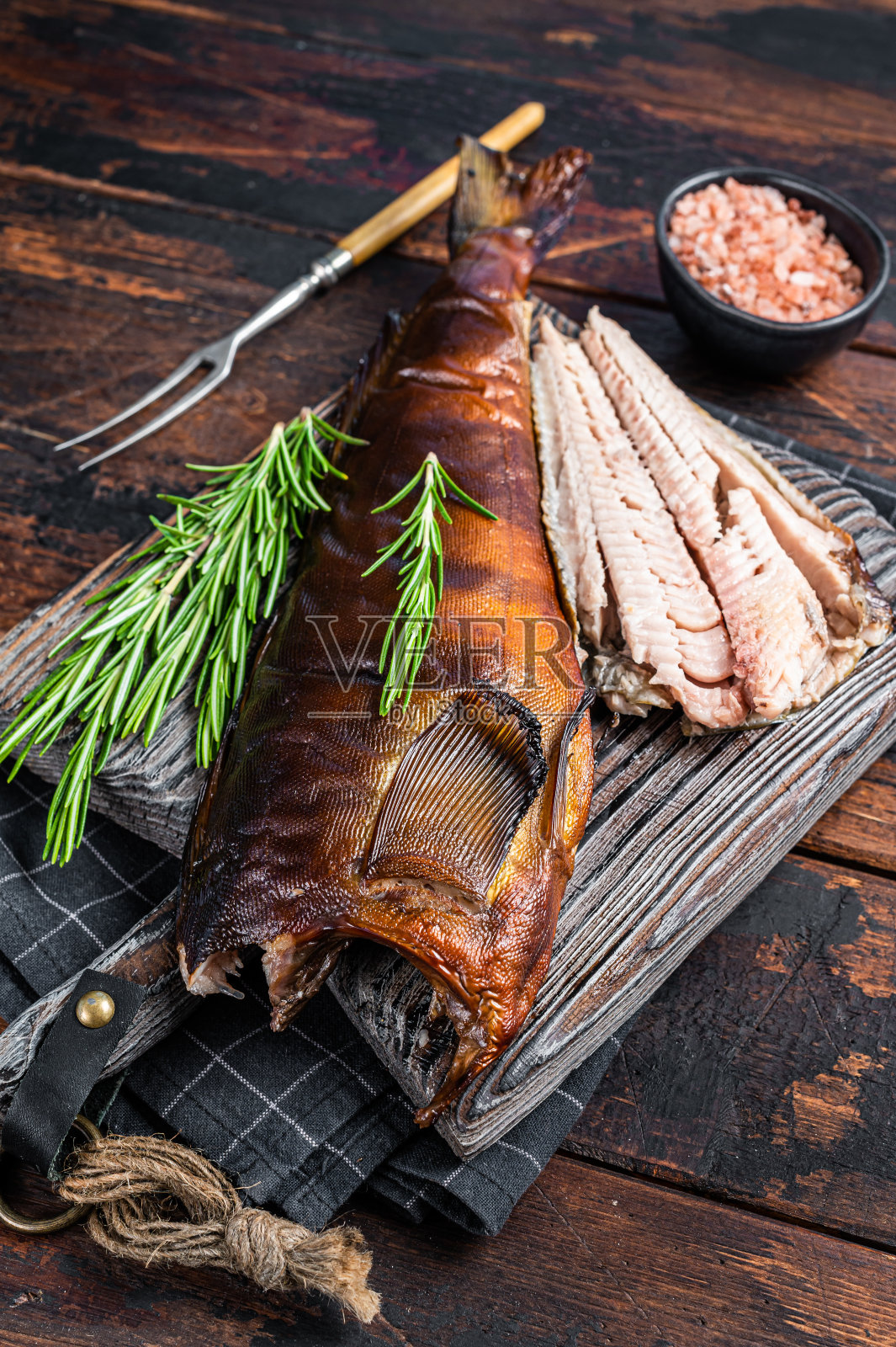 用迷迭香将热熏鱼切在木板上。深色木制背景。俯视图照片摄影图片
