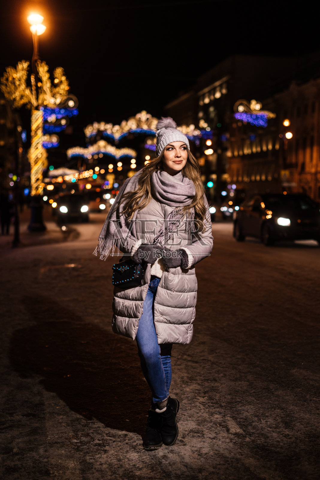 美丽的年轻女子穿着暖和的衣服在城市的街道上，背景是模糊的城市灯光和汽车照片摄影图片
