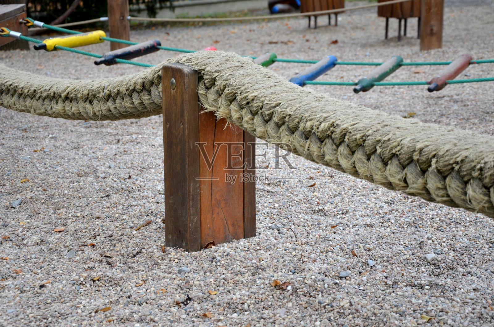 操场上五颜六色的绳梯低低地伸展在几个柱子之间。这孩子试图像平衡木一样在笨拙的障碍上行走。会和沙子或鹅卵石一起掉落吗照片摄影图片