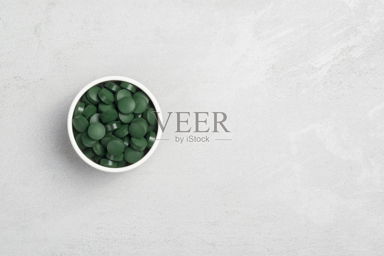 一个灰色背景上放着螺旋藻片的碗，一个放文字的地方照片摄影图片