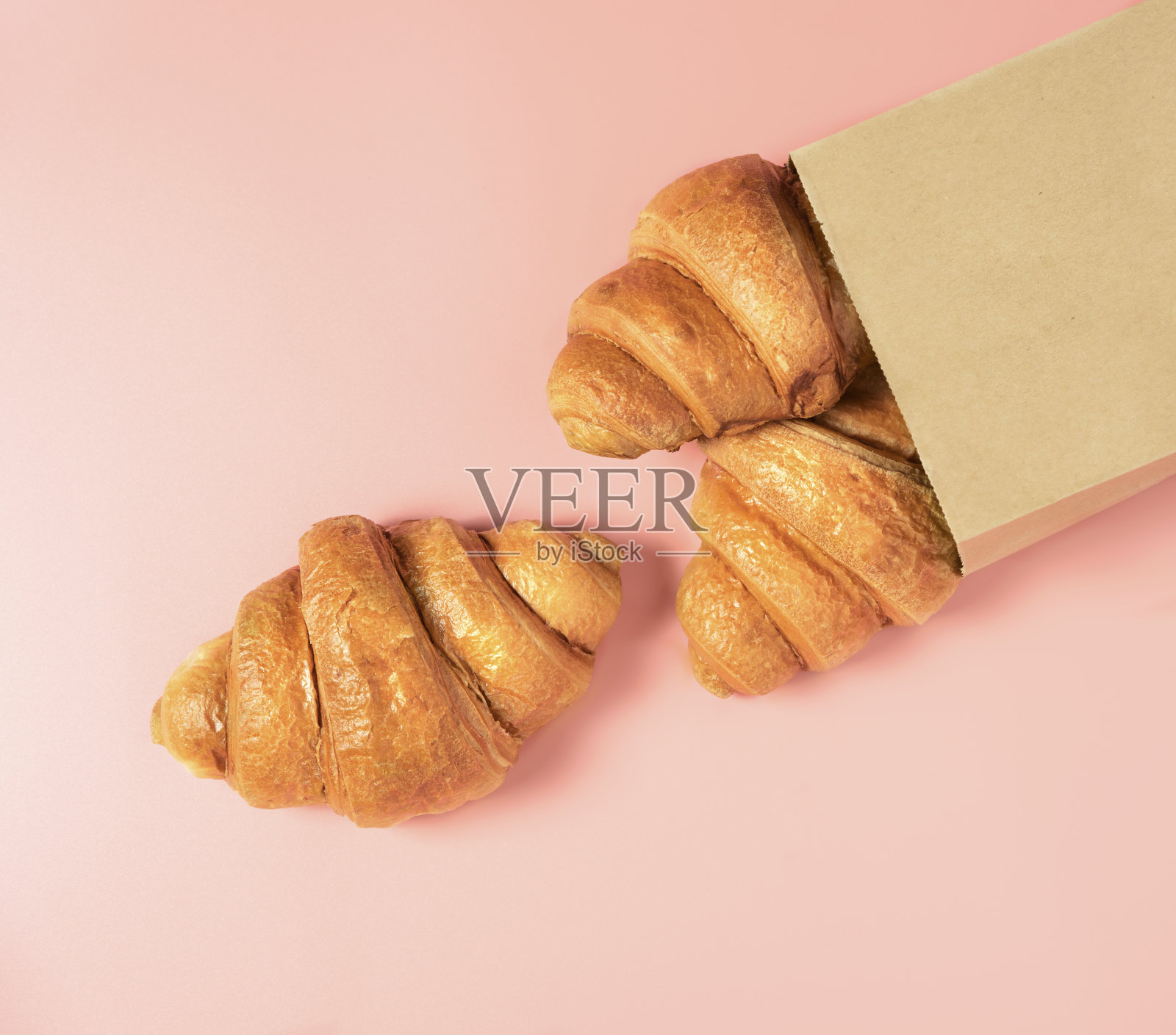 三个法国羊角面包装在粉色背景的纸袋里。照片摄影图片