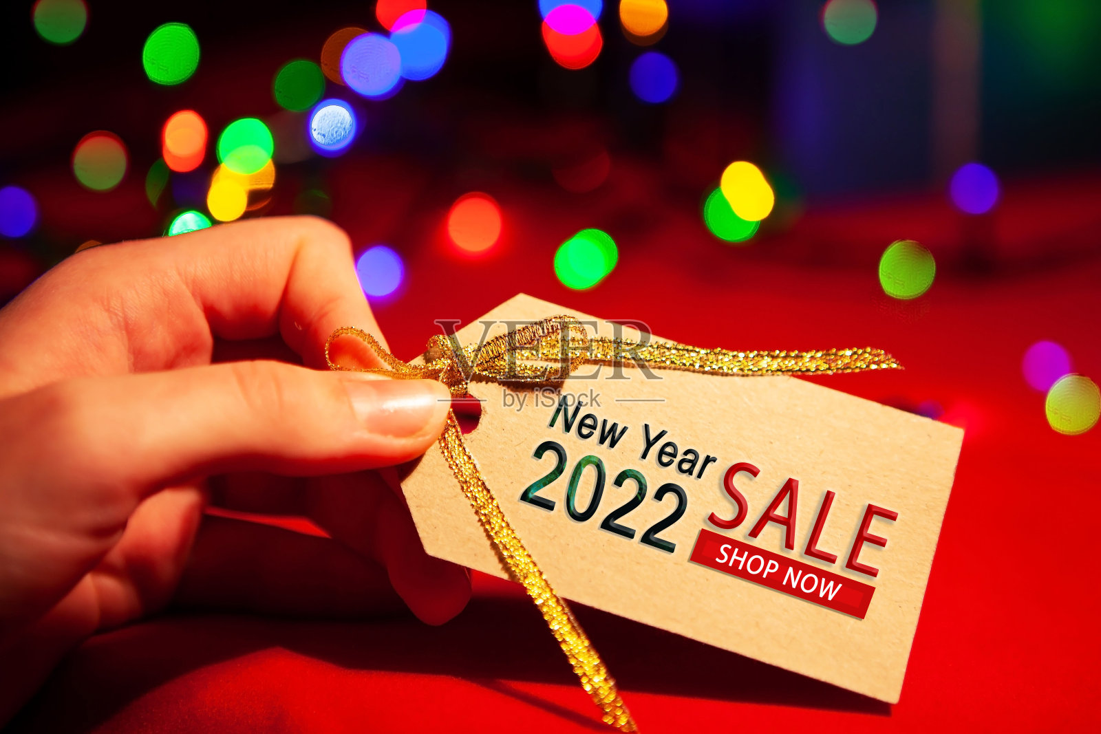 一位妇女手里拿着一个标签，上面写着:“2022年新年大甩卖，现在购物。”在一个红色的背景，与一个多色的格兰德。照片摄影图片