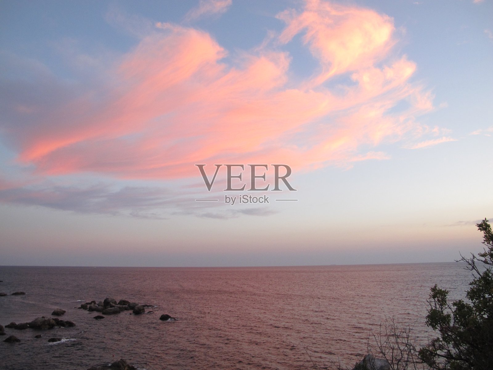 在一个阳光明媚的夏日夜晚，粉红色的云映衬着蓝色的大海和天空照片摄影图片