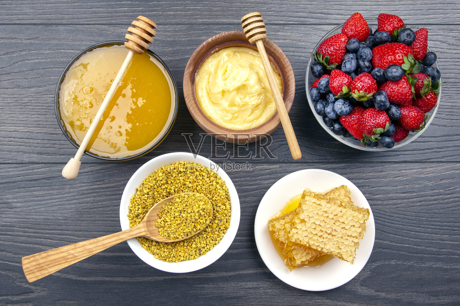 新鲜的蜂蜜，坚果，草莓和蓝莓在木制背景。健康有机维生素食品。照片摄影图片