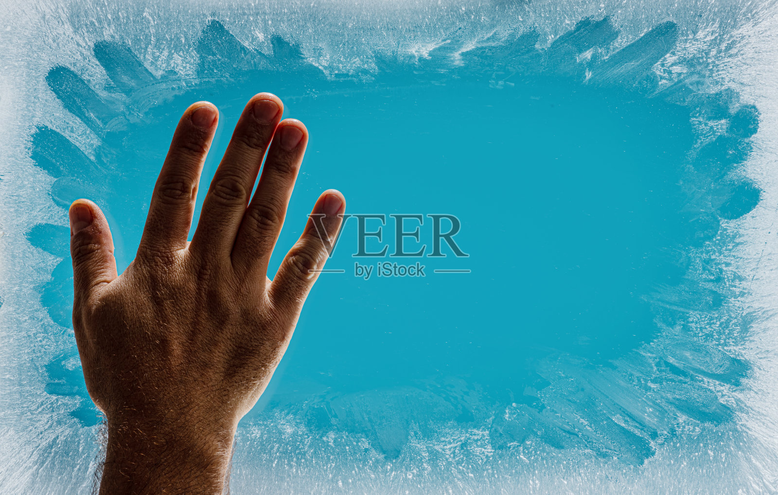 霜冻的冬天窗户上的霜冻图案是圣诞节奇迹的象征。男人的手擦去了窗户中央的霜冻图案。圣诞节或新年背景。照片摄影图片