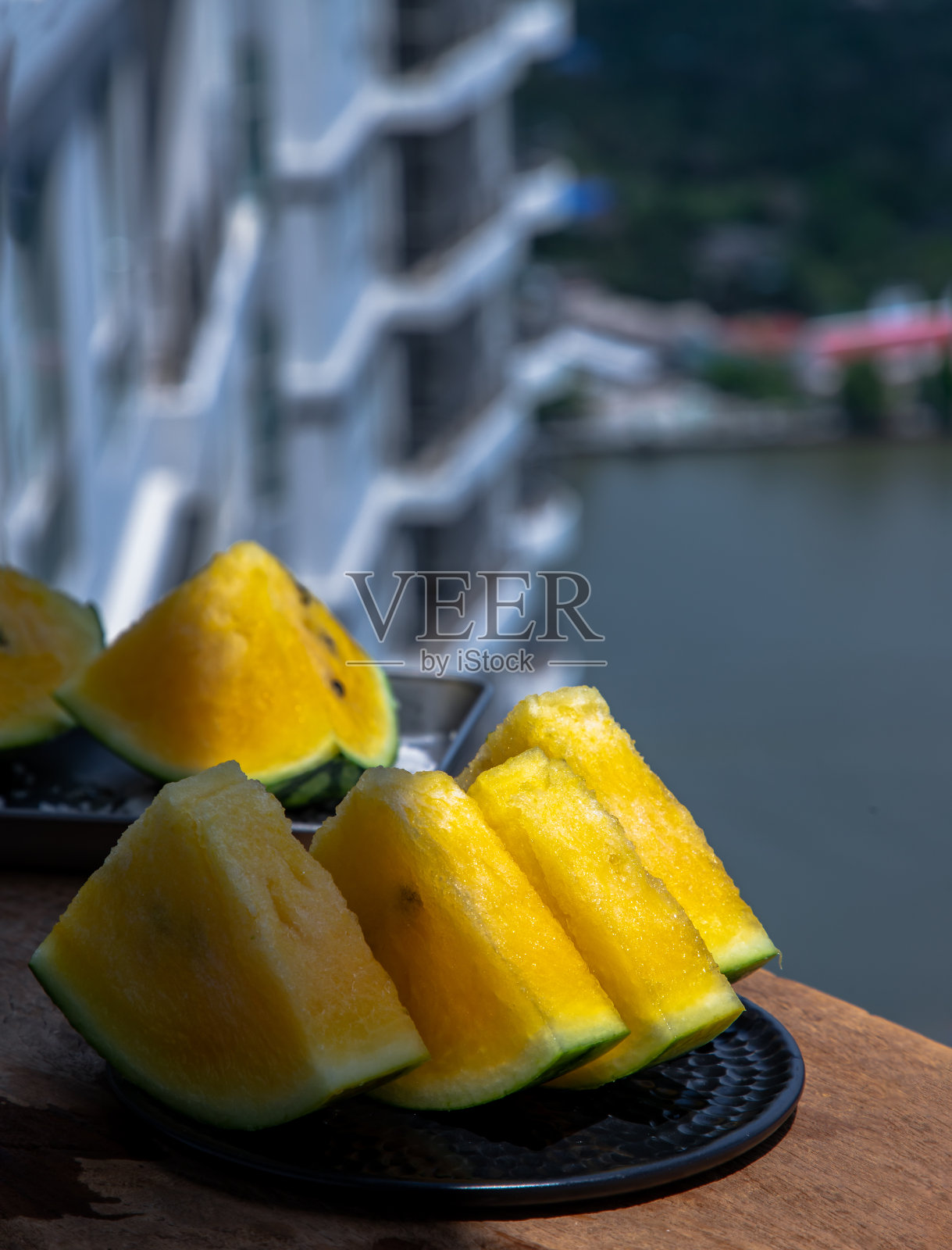 新鲜多汁的黄色西瓜切成三角形在圆形盘子和背景建筑物和城市景观。照片摄影图片