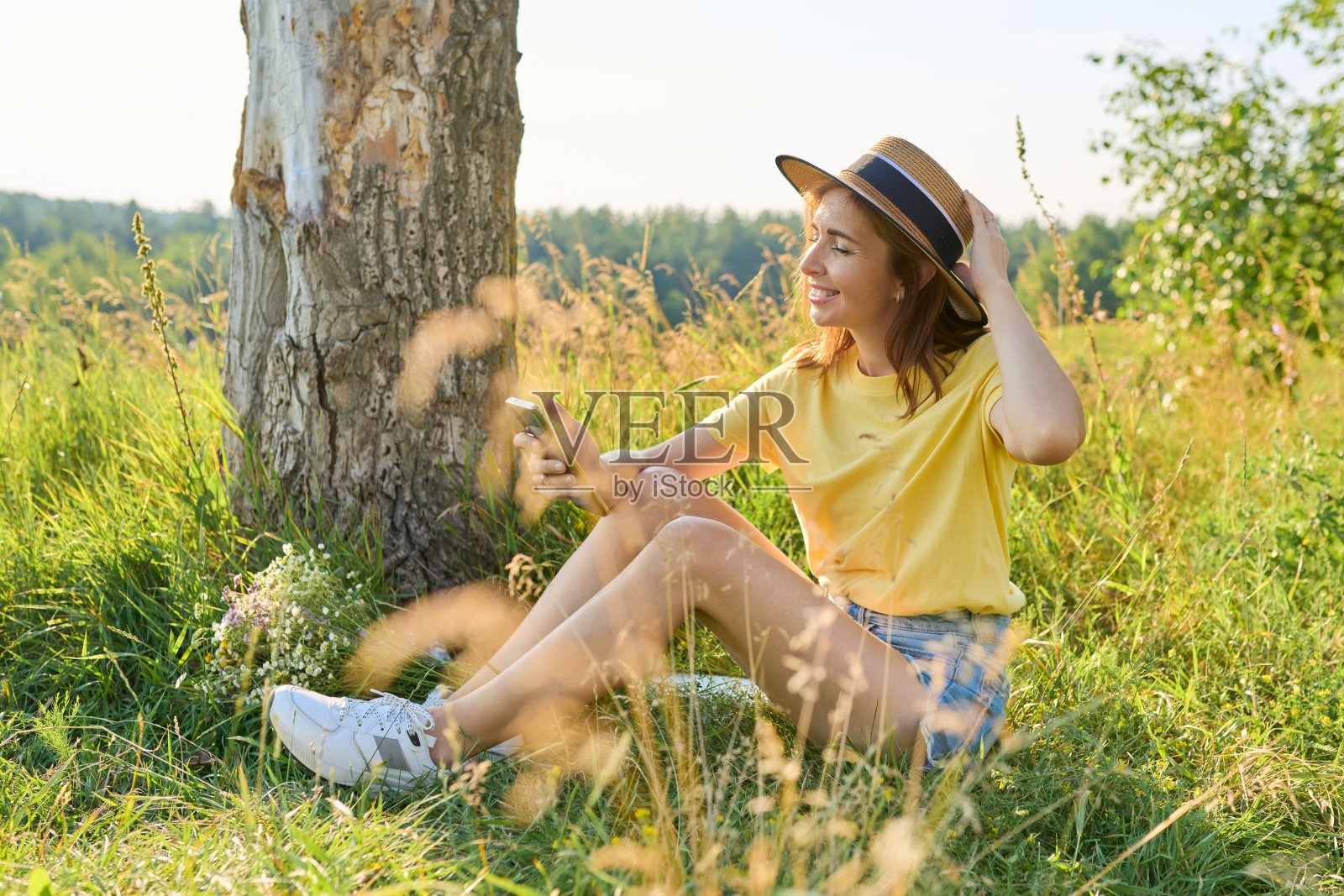 快乐的成年女性坐在草地上，休息，使用智能手机照片摄影图片