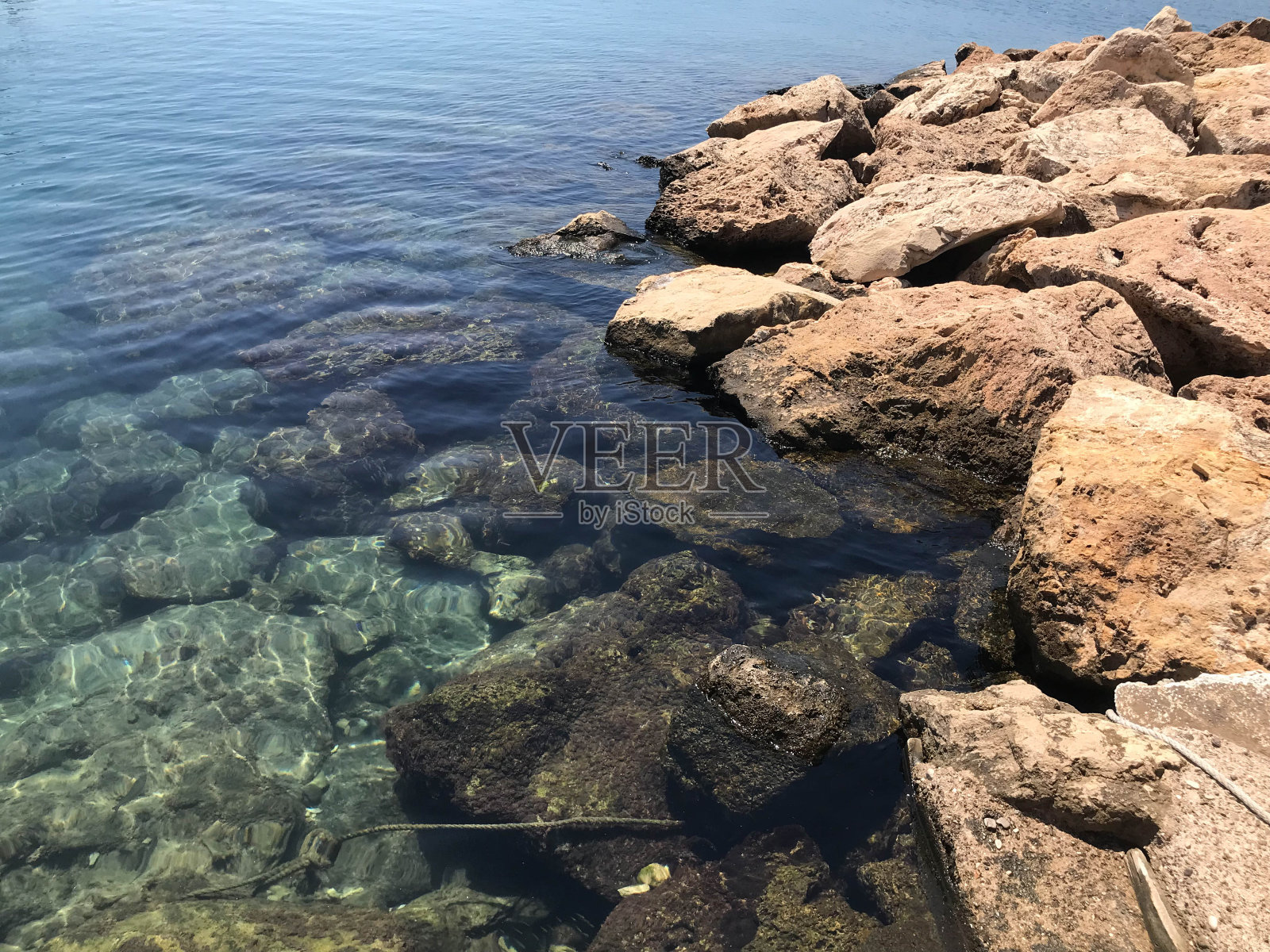 清澈的水面上有许多彩色的大石块。一个白色的泡沫浪卷到岸边，冲刷着几块黑色的大石头，映衬着灰蓝色的海水照片摄影图片