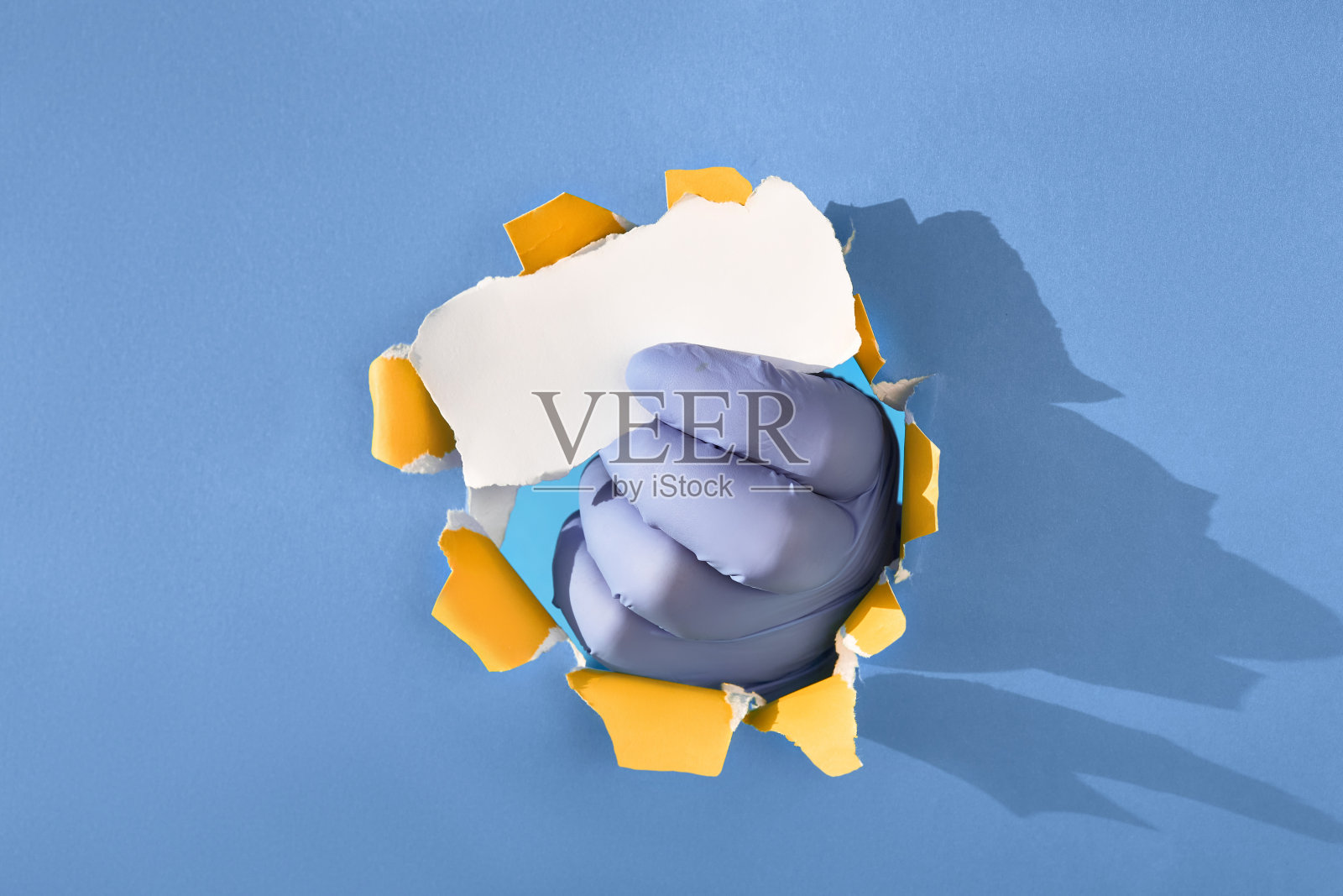 将手伸进手套的纸孔中，夹住撕破的纸。复制空间，将文本放在蓝纸上照片摄影图片