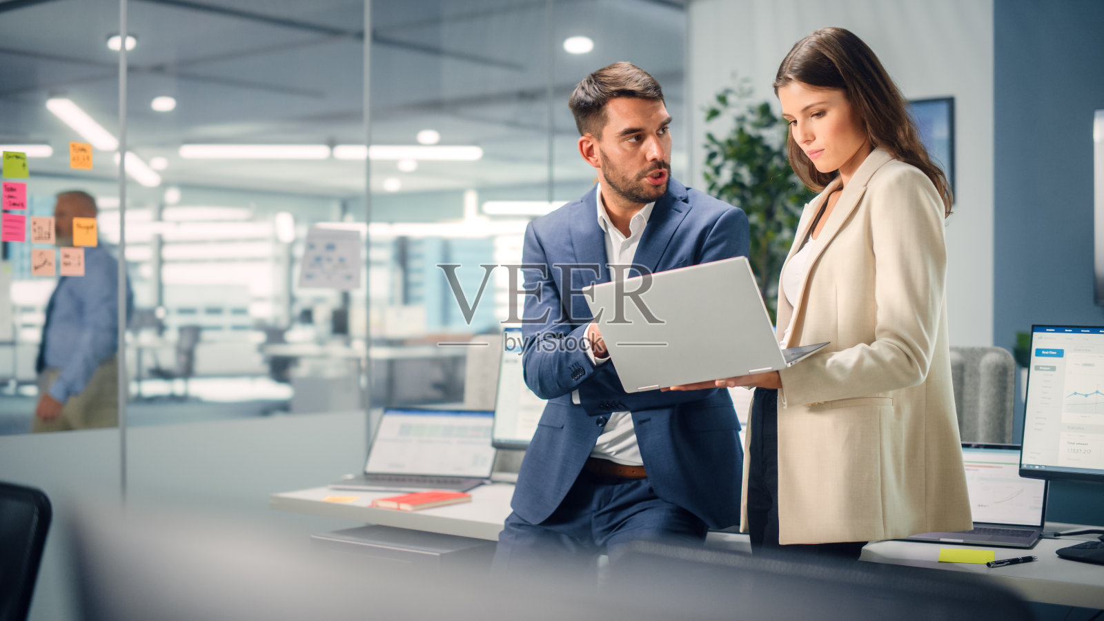 年轻经理在办公室使用笔记本电脑时与有经验的同事交谈。同事们讨论商业、金融和市场项目。专家在多样化的团队中工作。照片摄影图片