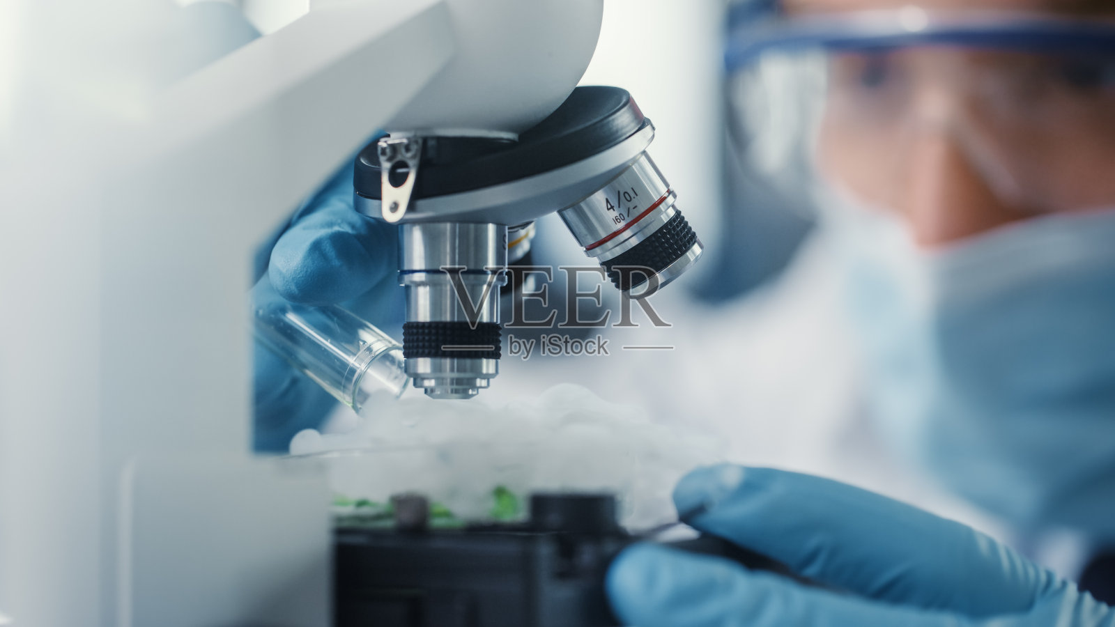 显微镜下戴医用口罩和安全眼镜的男科学家在混合绿色化学液体的特写镜头。微生物学家在现代化实验室和技术设备中工作。照片摄影图片