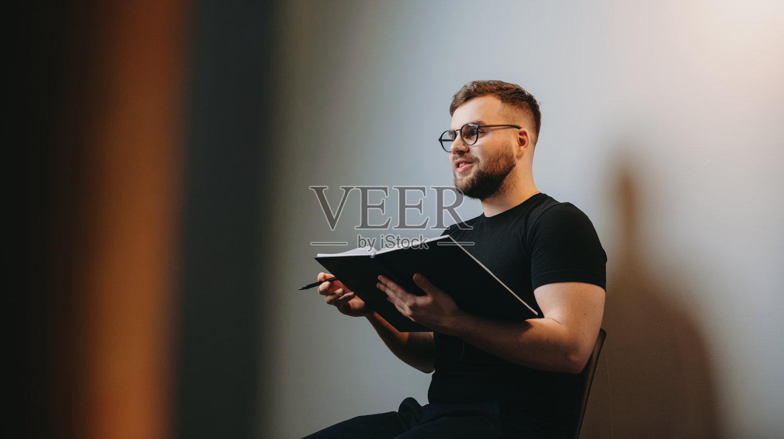 一个男人坐在椅子上，手里拿着一个笔记本，和别人说话。微笑的人。孤立。照片摄影图片