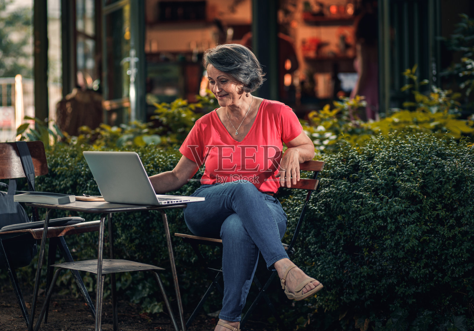 资深女性坐在户外咖啡厅使用笔记本电脑。照片摄影图片