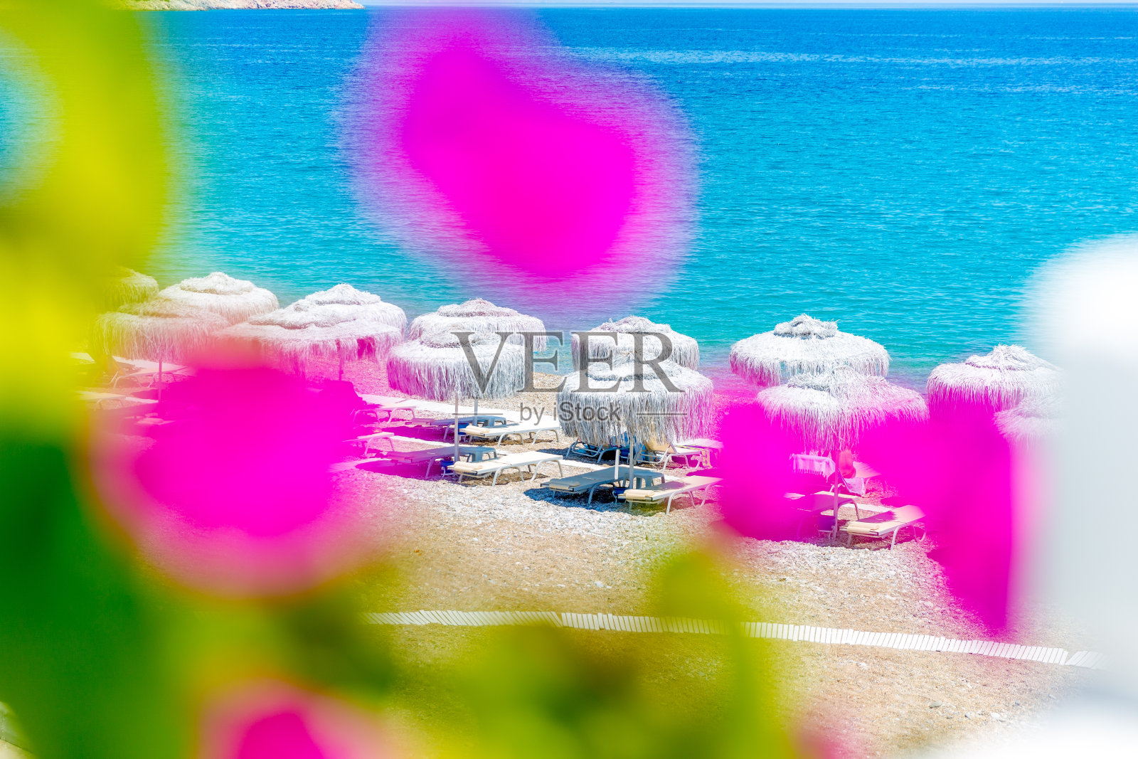 深蓝色的大海在阳光床后面伸展，沙滩伞在模糊的花朵后面，是一个美妙的海滩，唤起无限的感觉和度假时，你看天际线。照片摄影图片