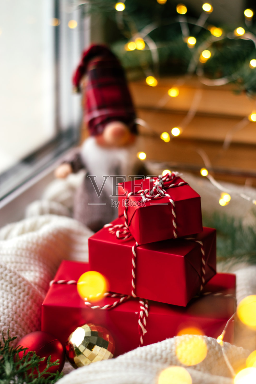 一个北欧小矮人玩具和红色的礼品盒放在节日装饰的窗台上。新年和圣诞节的概念。照片摄影图片