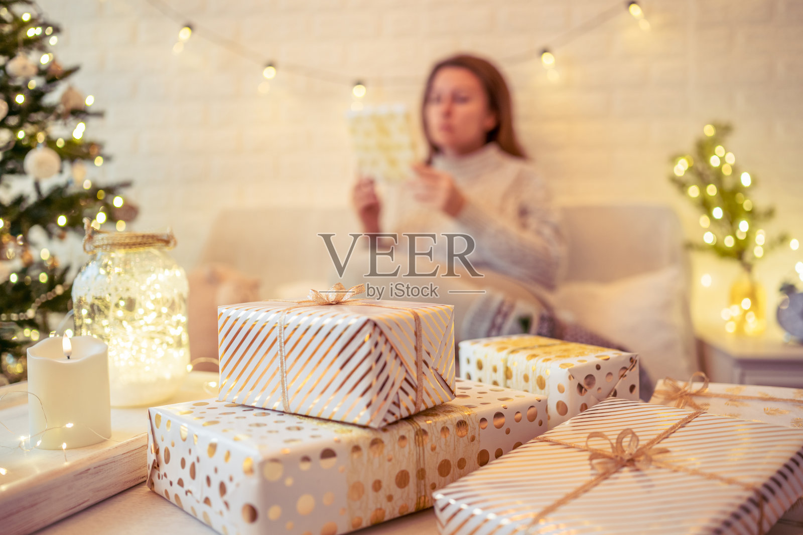 一位女士坐在圣诞树旁的沙发上，把手工制作的礼盒放在桌子上。提出了家庭。照片摄影图片