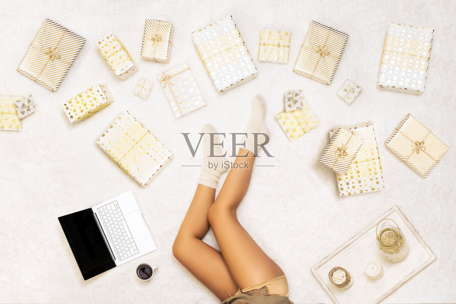 圣诞节销售,折扣。在线购物。一位女士用笔记本电脑下单、买礼物，坐在雪白的地毯上，旁边是许多包装好的盒子。前视图。概念照片摄影图片