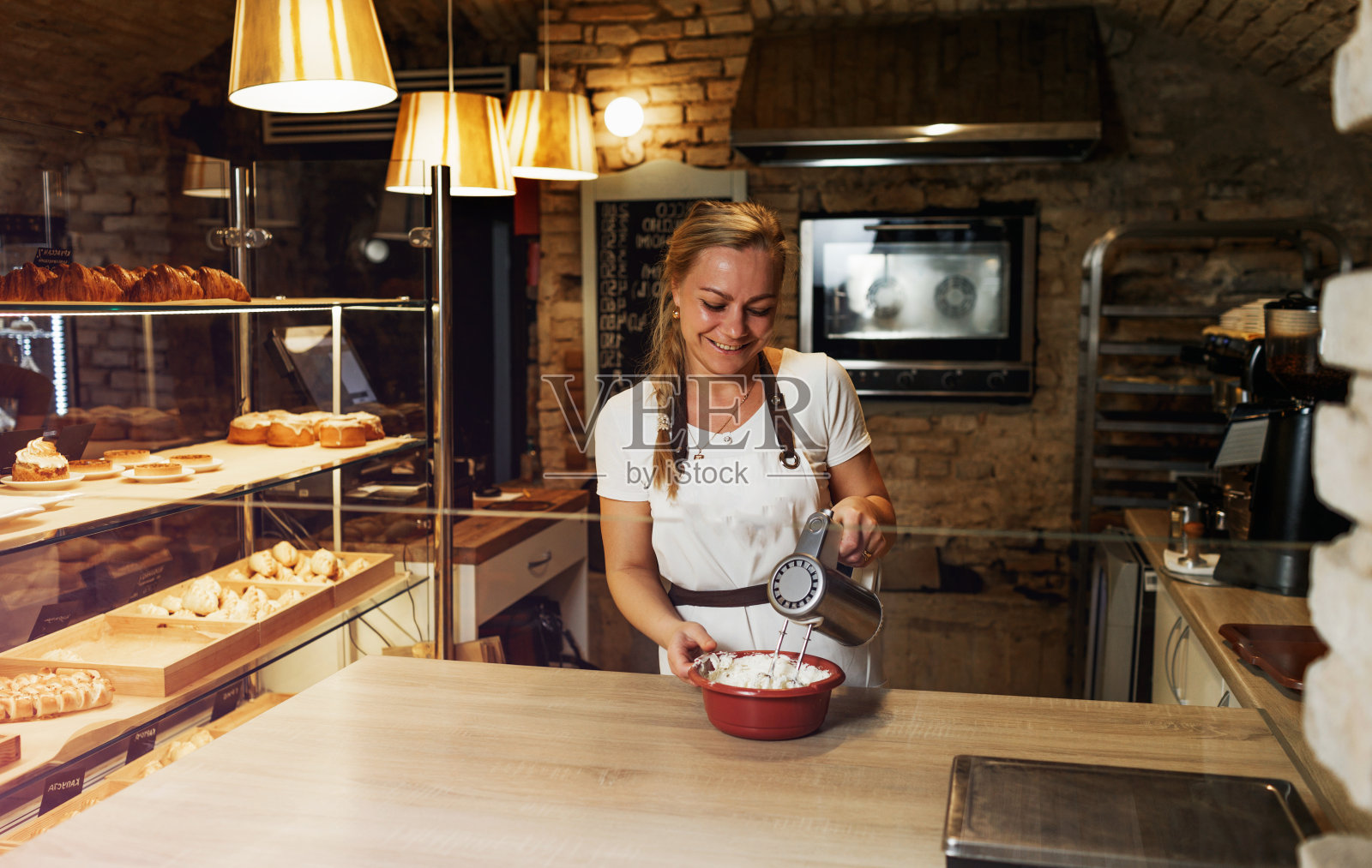 那个女孩用电动搅拌器搅打蛋白奶油。开放式厨房的咖啡馆照片摄影图片