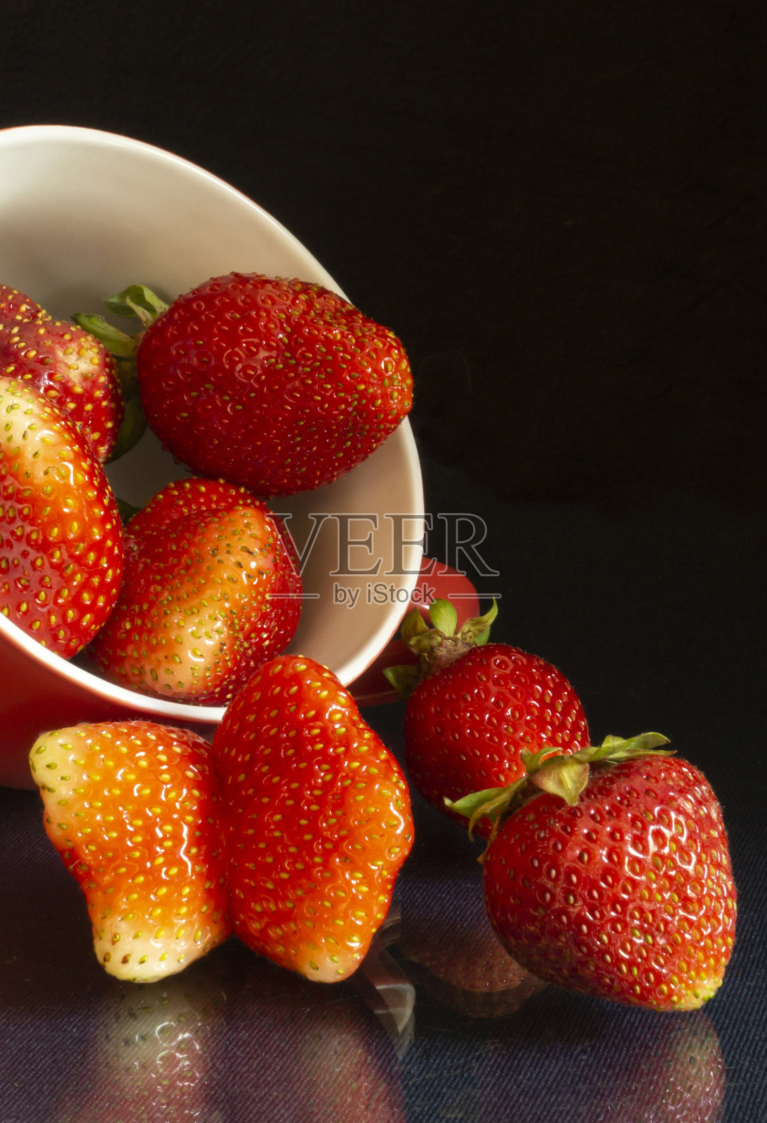 草莓在杯子上的黑色背景和桌子上的反射。照片摄影图片