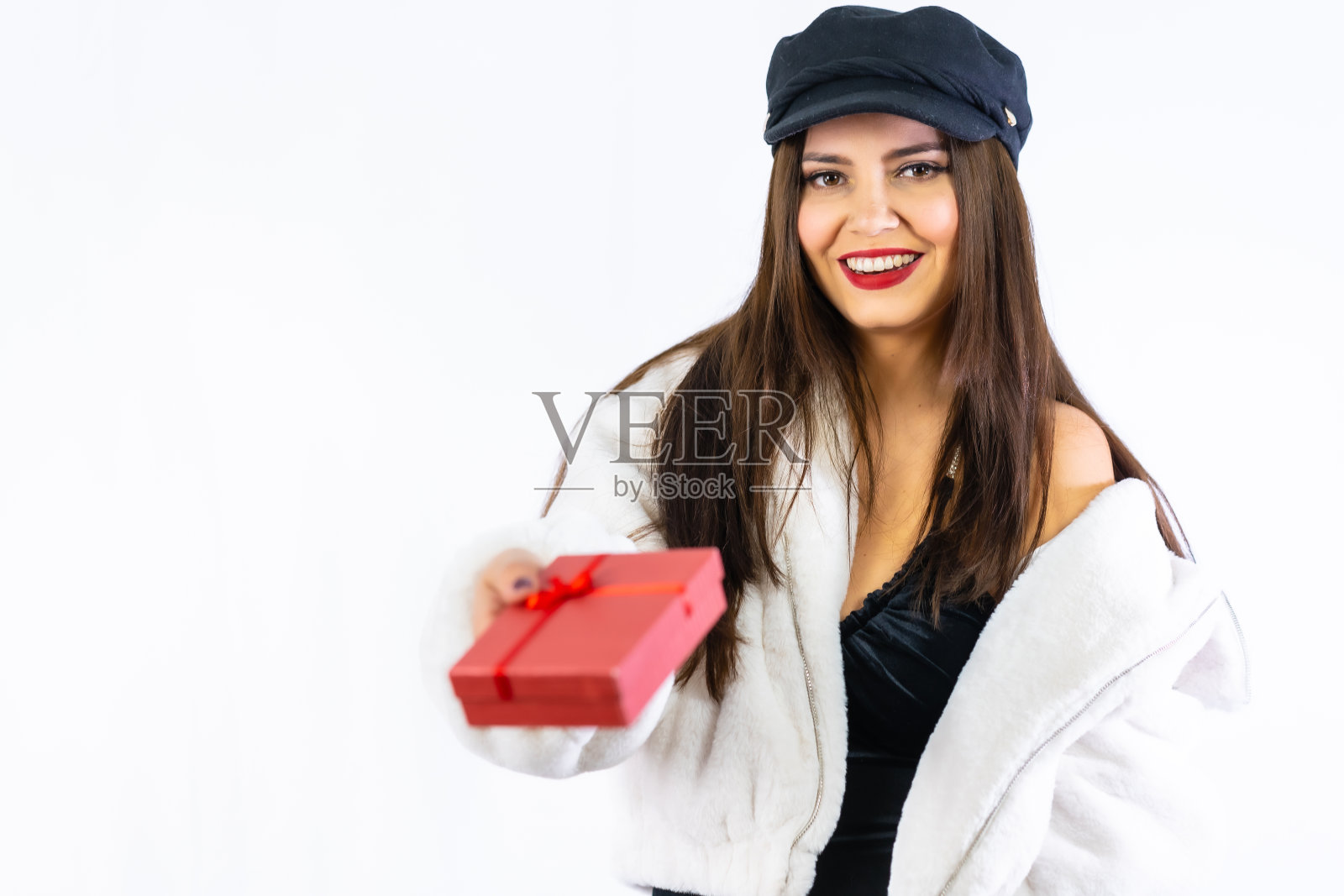 一个年轻的拉丁黑发女孩的手在白色背景上快乐地递上一份礼物。肖像给模特一个红色的礼品盒照片摄影图片