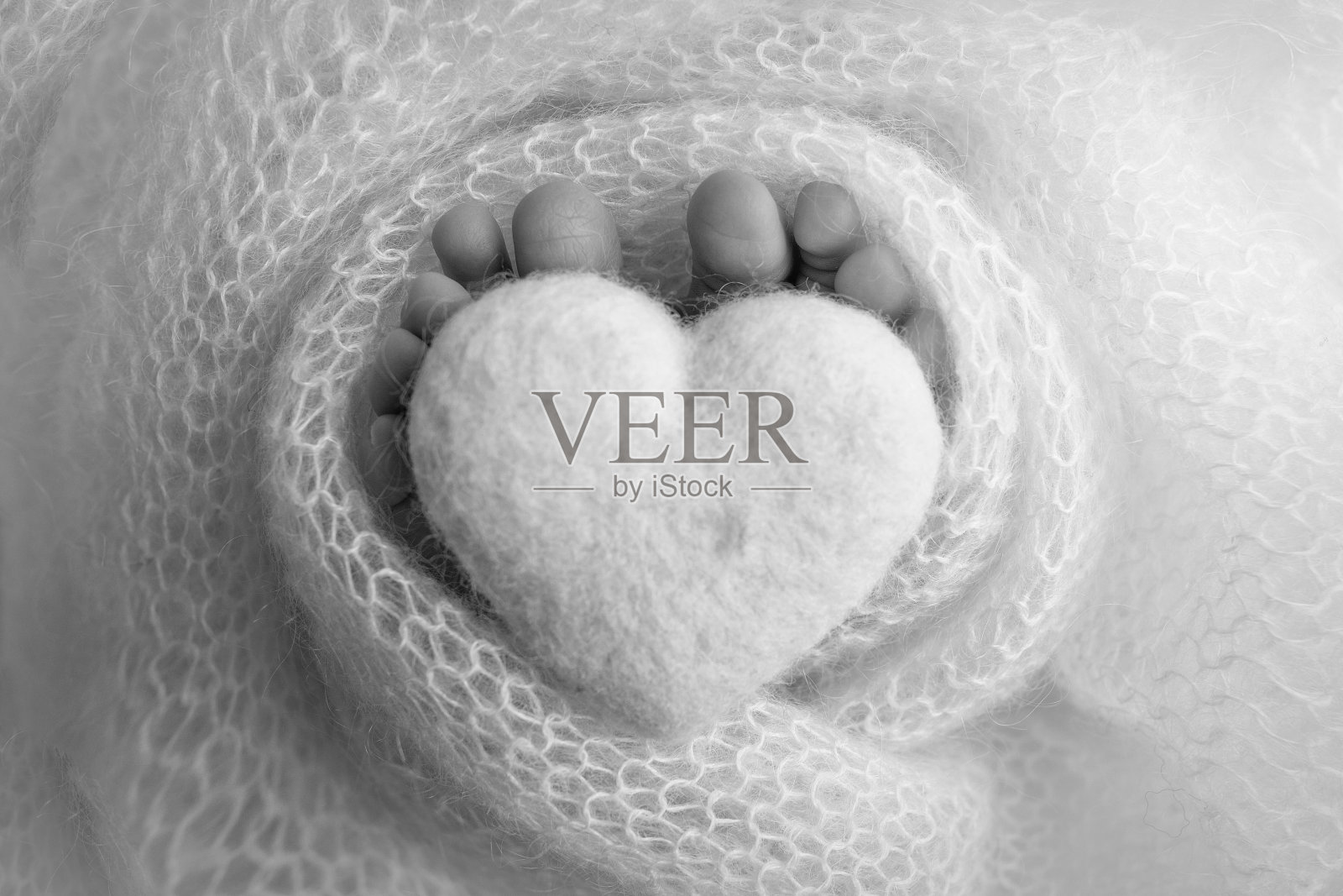 新生儿的小脚。柔软的双脚裹在羊毛毯里。靠近一个新生儿的脚趾，脚跟和脚。把心脏编织在婴儿的腿上。微距摄影工作室。黑色和白色。照片摄影图片