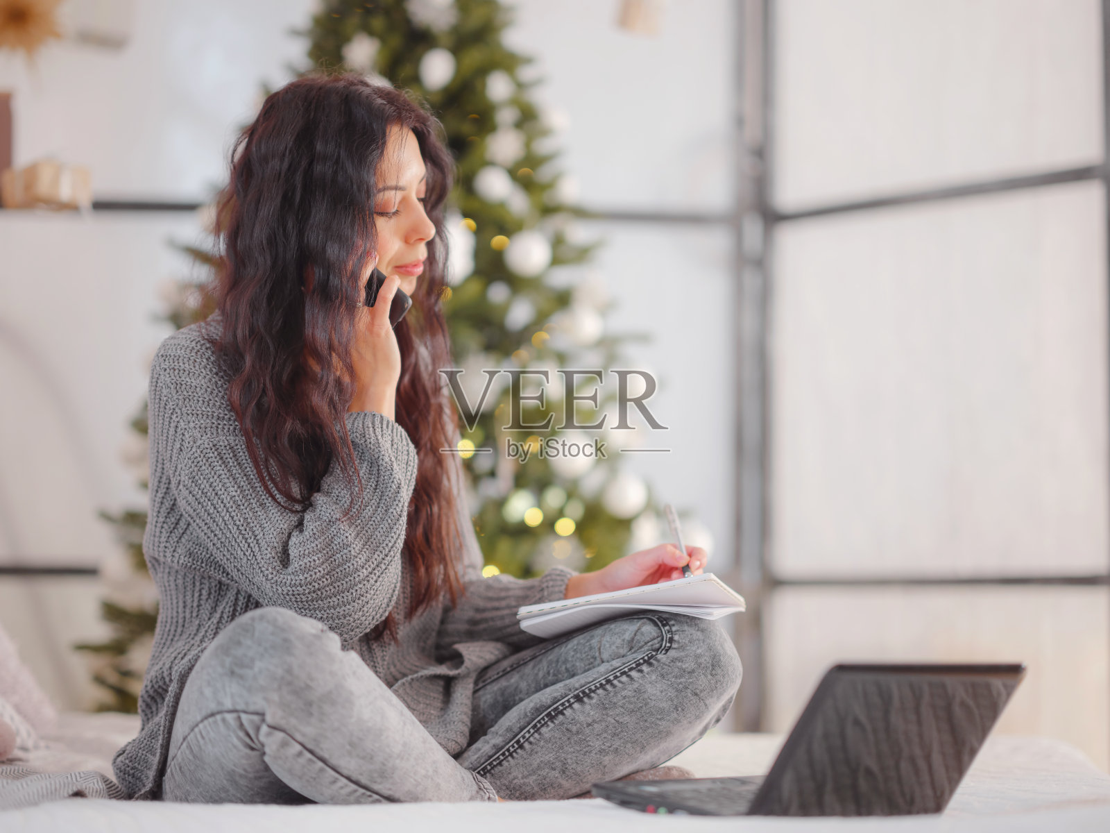 女人在舒适的灰色针织毛衣在床上使用笔记本电脑，圣诞节假期照片摄影图片