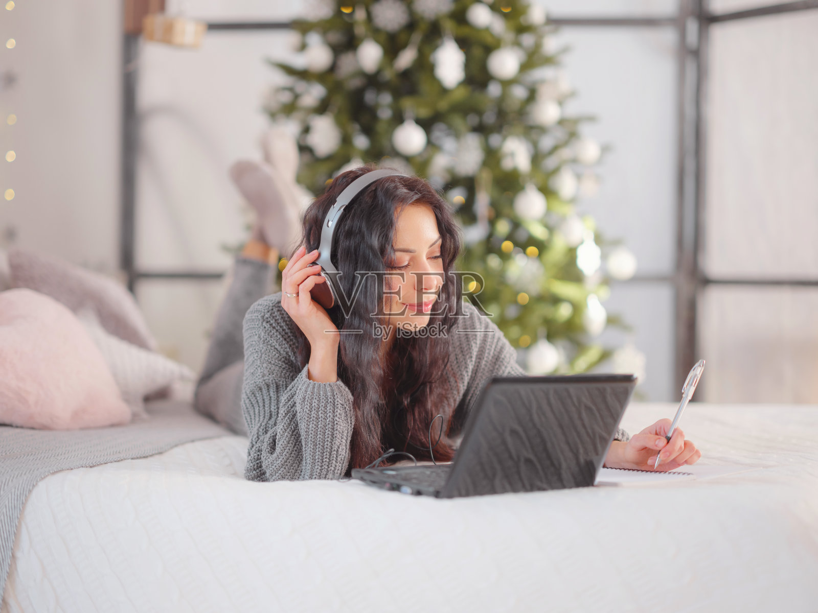 女人在舒适的灰色针织毛衣在床上使用笔记本电脑，圣诞节假期照片摄影图片