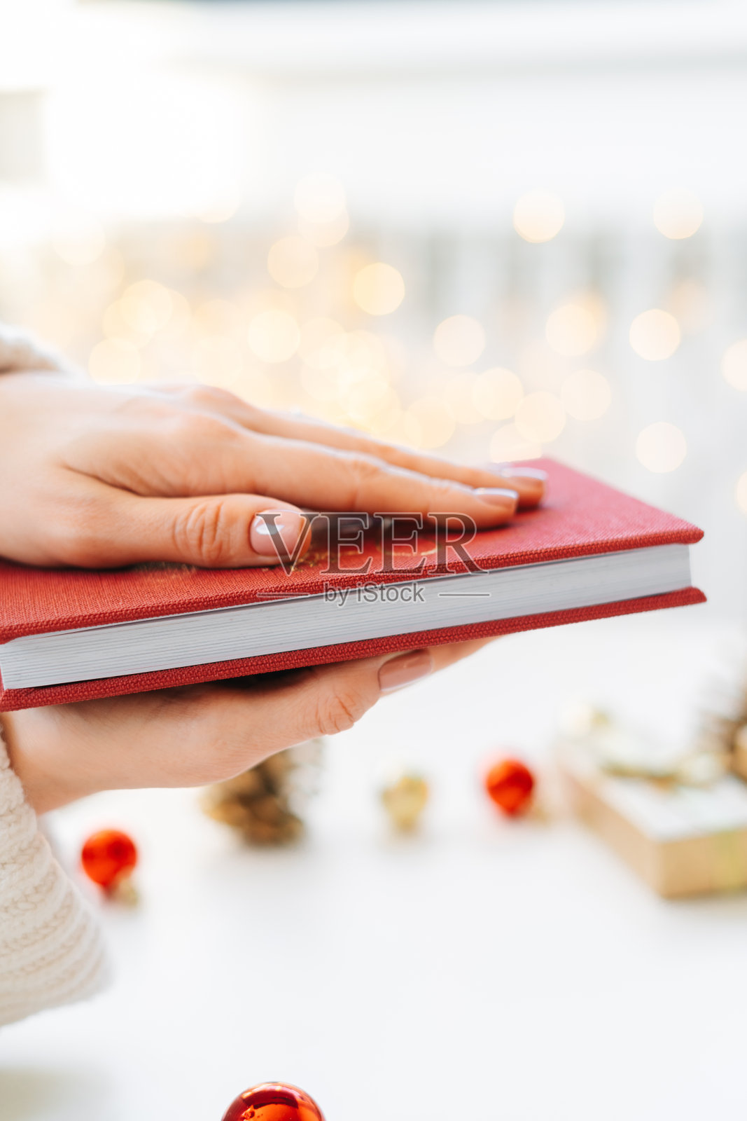 一个小女孩手里拿着一本红书，背景是礼物和圣诞玩具，一个花环。圣诞节的概念照片摄影图片