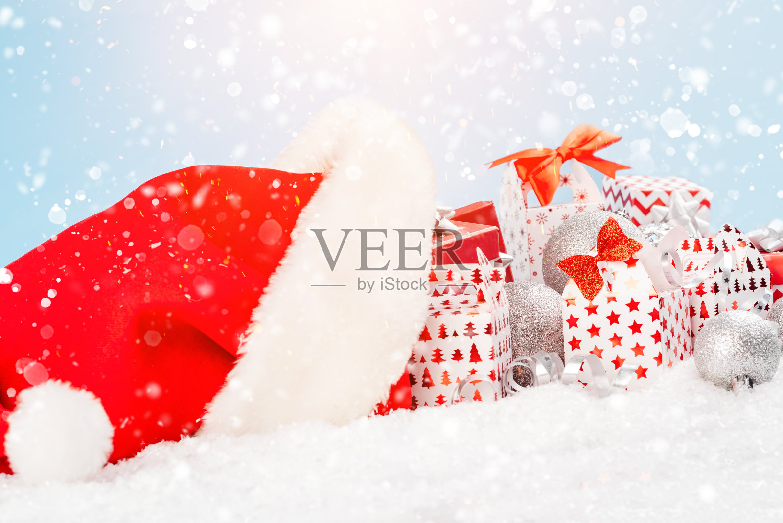 圣诞老人的帽子躺在雪地里，在浅蓝色背景上的各种各样的盒子里装满了新年的节日礼物。新年的概念。圣诞贺卡。照片摄影图片
