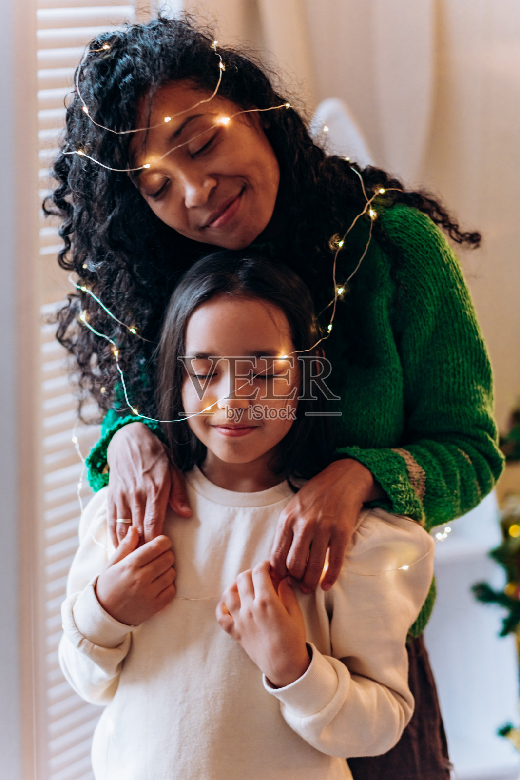 小女孩和妈妈戴着花环对着圣诞树摆姿势照片摄影图片
