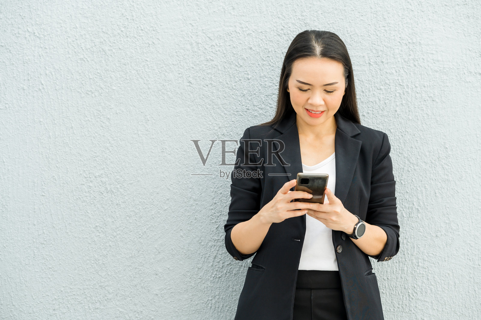 身穿黑色西装，手持连接互联网发送招聘信息的手机的亚洲职业女性的肖像。在日常生活中使用互联网技术的概念照片摄影图片