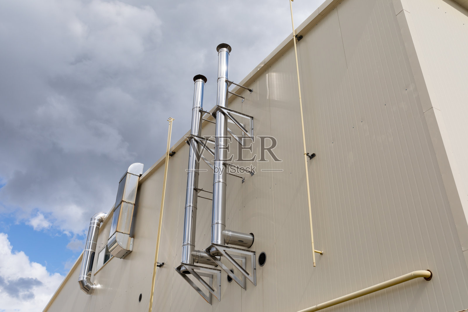 工业建筑外墙上闪亮的金属烟囱，映衬着多云的天空背景。照片摄影图片