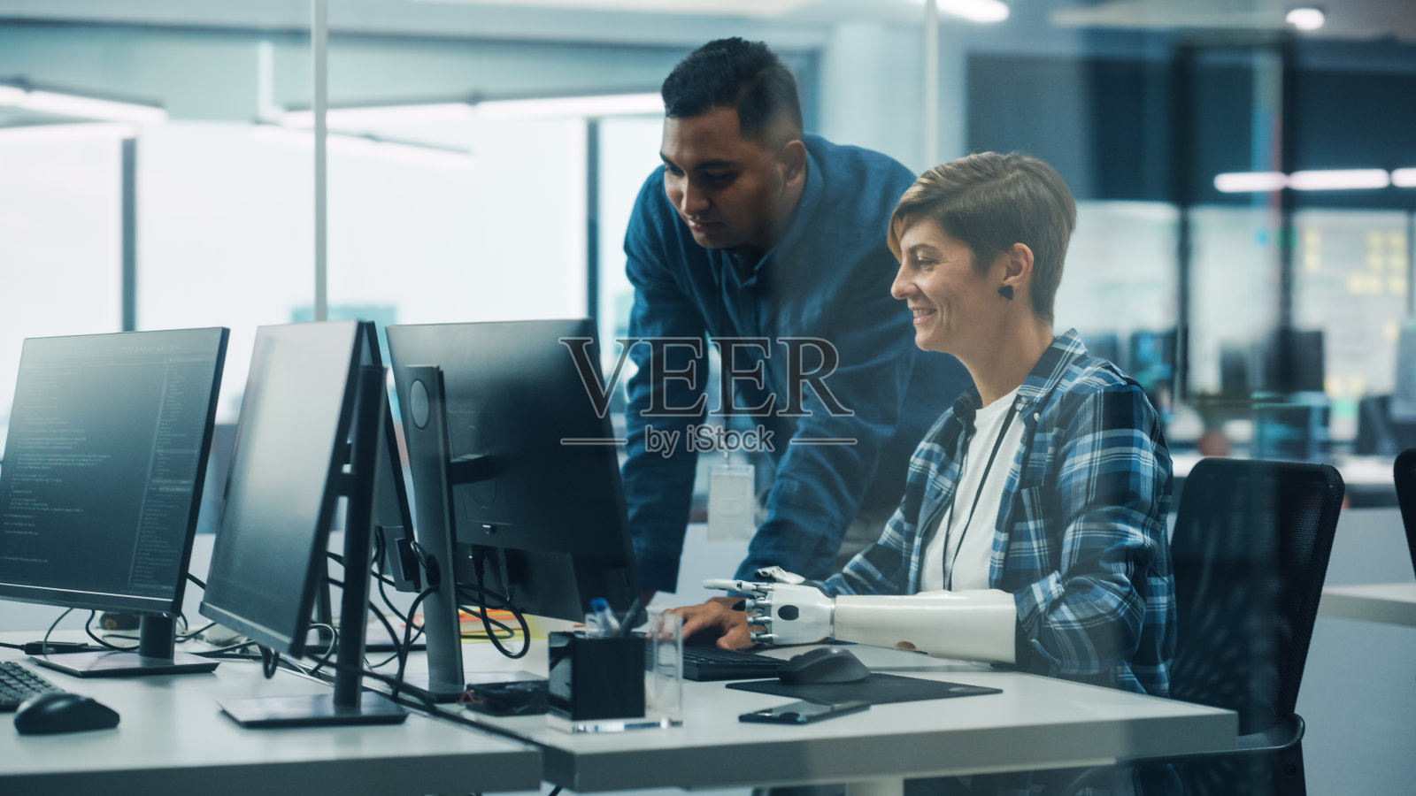 多元化包容性办公室的团队合作:项目经理与带假肢的残疾妇女在台式电脑上工作。专业软件工程师创建电子商务应用解决方案照片摄影图片