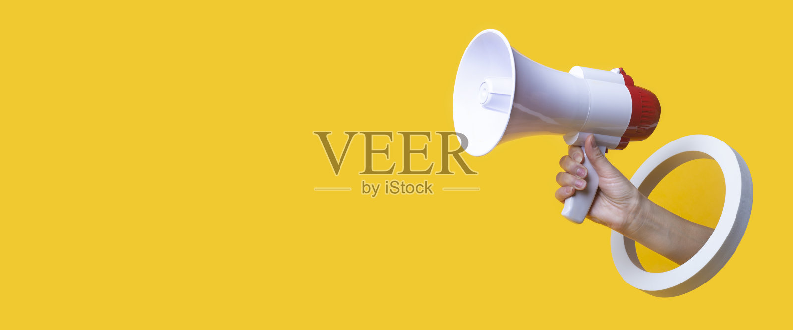 在黄色背景上，一只女性手拿着一个圆孔中的扩音器。横幅。照片摄影图片