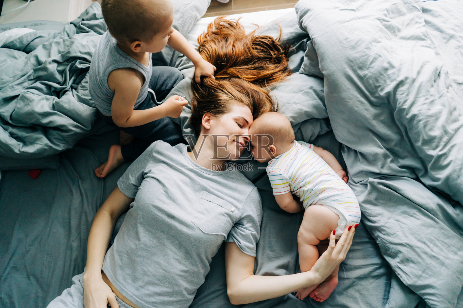 早上，妈妈带着两个小孩躺在床上，享受着亲子关系和母爱照片摄影图片
