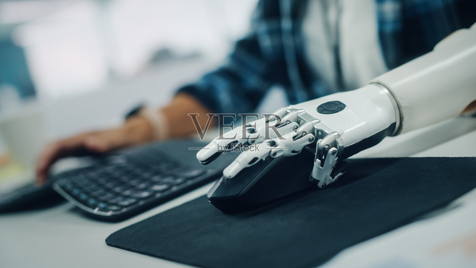包容性办公室:残疾人士使用假臂在电脑上工作。专业配备先进的肌电仿生肢体控制鼠标。以荷兰角度聚焦双手照片摄影图片
