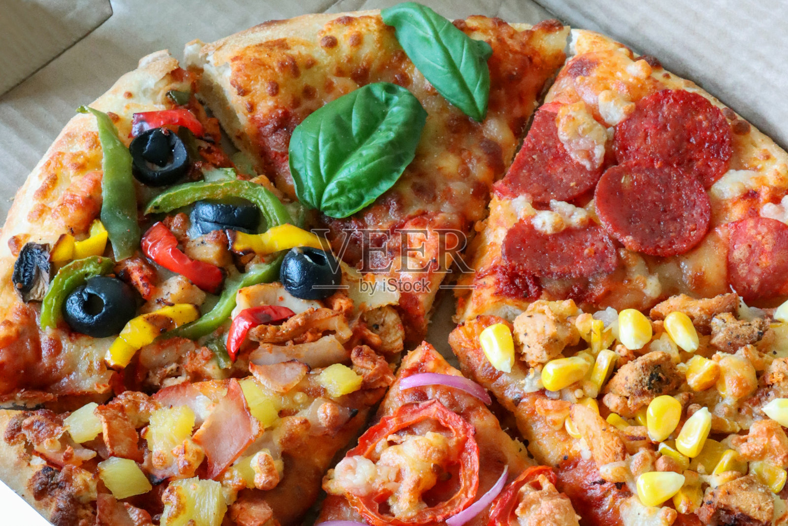 全帧图像纸箱外卖披萨片有各种各样的浇头，包括意大利辣香肠，玛格丽特，夏威夷披萨，融化的金色水牛马苏里拉奶酪，番茄marinara酱，升高的视野，重点前景照片摄影图片