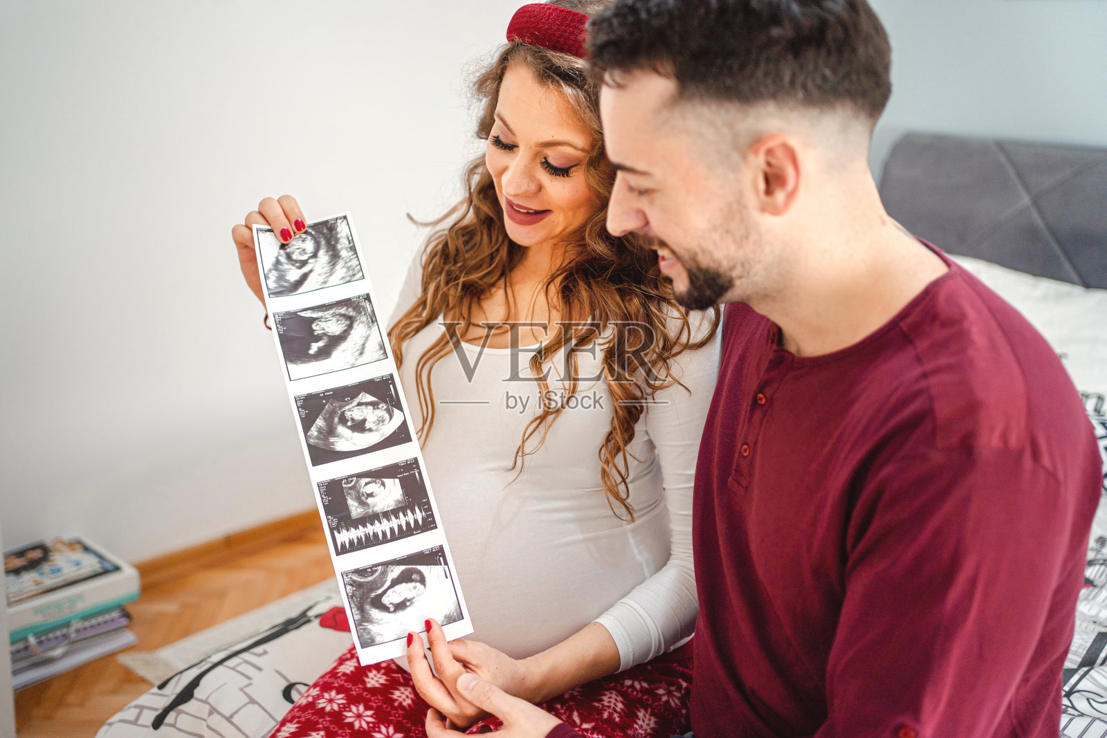 未来的父母坐在床上看着他们未来宝宝的超声波照片摄影图片