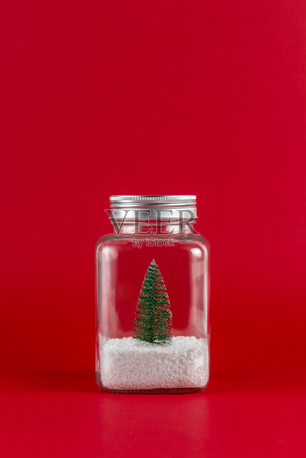 绿色的圣诞树与雪在一个玻璃罐里在红色的背景。最小的圣诞节或新年假期概念。照片摄影图片