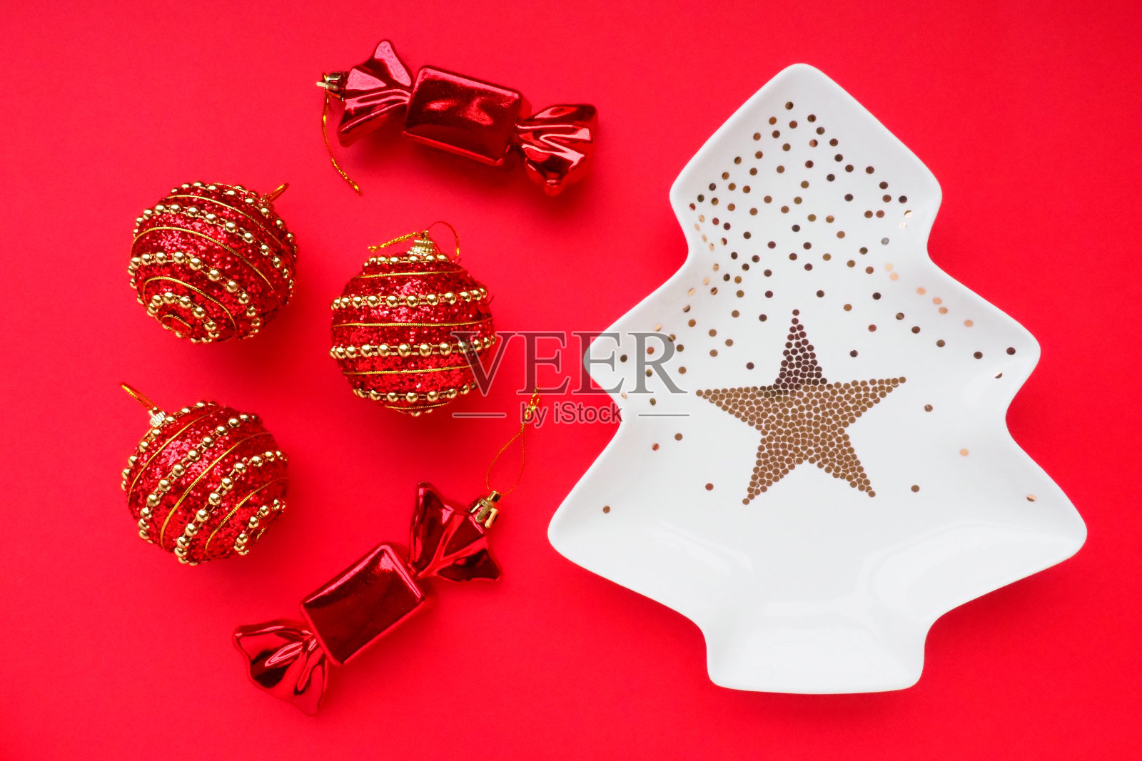 圣诞树上挂着金饰，中间有一颗星星。红色的背景。圣诞装饰和两颗甜糖果。三个带金色条纹的红球照片摄影图片