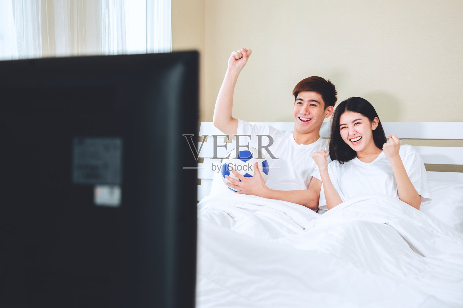 十几岁的夫妇躺在家里看电视电视体育足球足球比赛庆祝胜利的进球。照片摄影图片