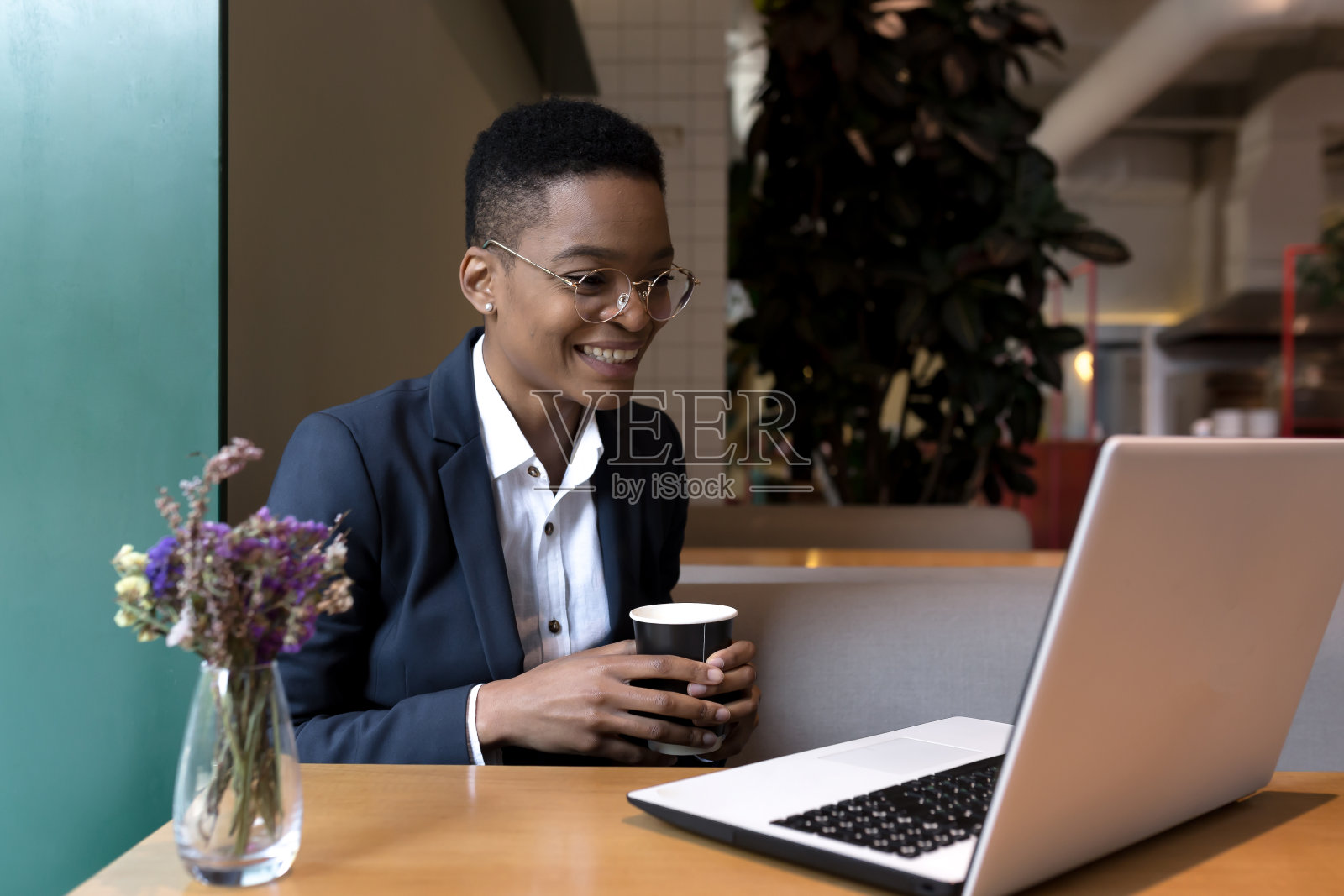 一个快乐的女人坐在咖啡馆里，喝着热饮，开着网络会议，打着视频电话，看着笔记本电脑的摄像头微笑着，午餐时分享着这个好消息照片摄影图片