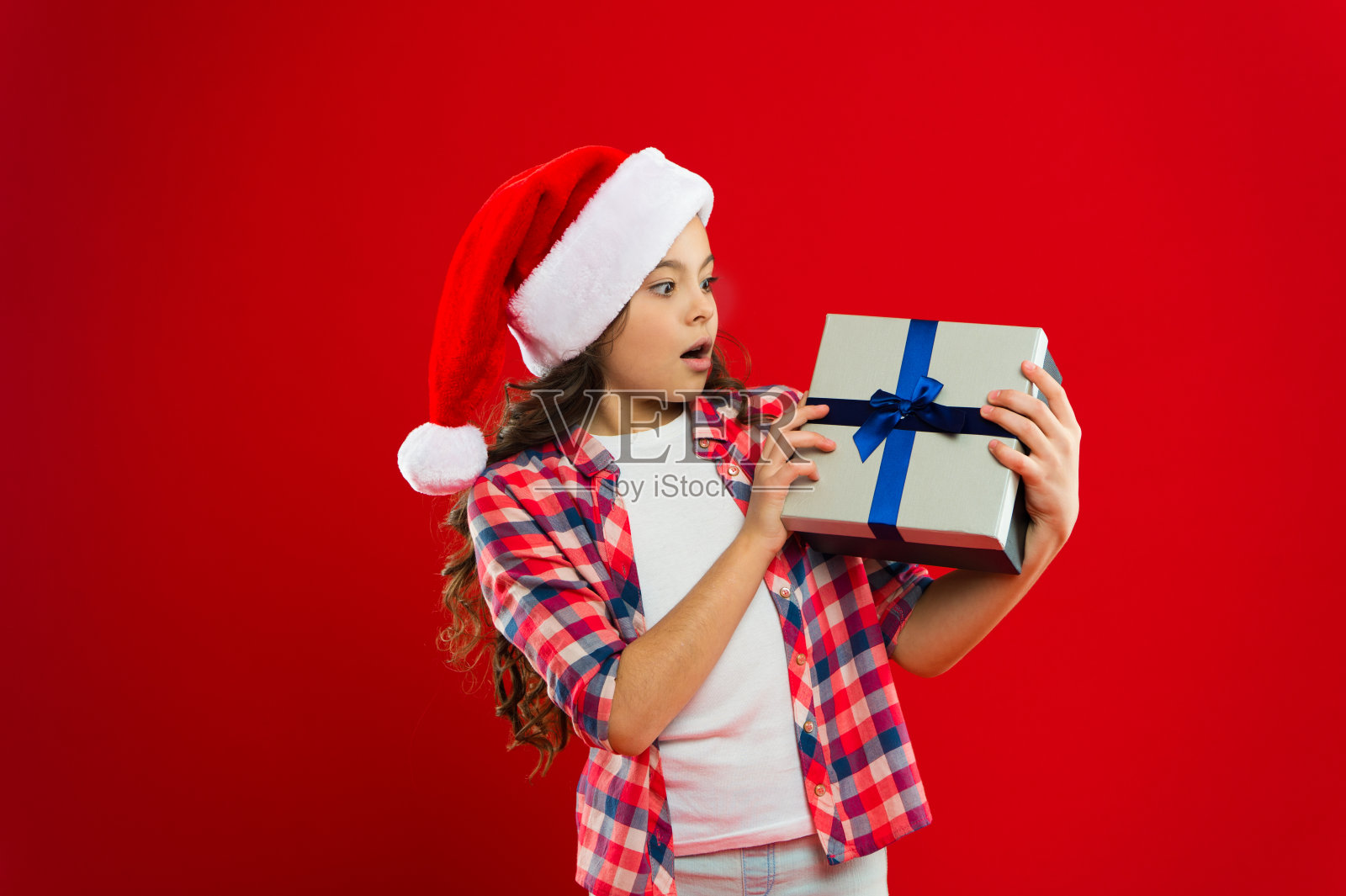 等待奇迹。圣诞购物。新年聚会。圣诞老人的孩子。快乐的寒假。小女孩。为圣诞礼物。的童年。戴着圣诞老人红帽的小女孩照片摄影图片