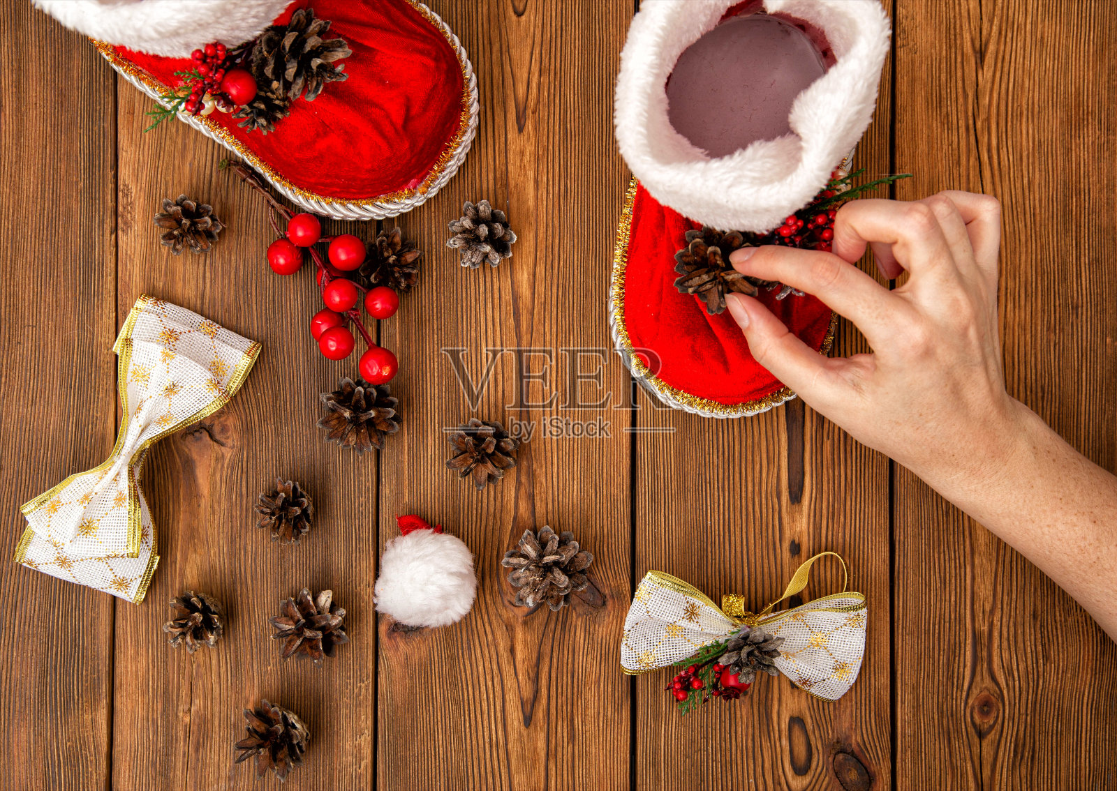 女孩为圣诞老人的新年红靴子做装饰品。女孩的手，木制的背景，圣诞照片摄影图片