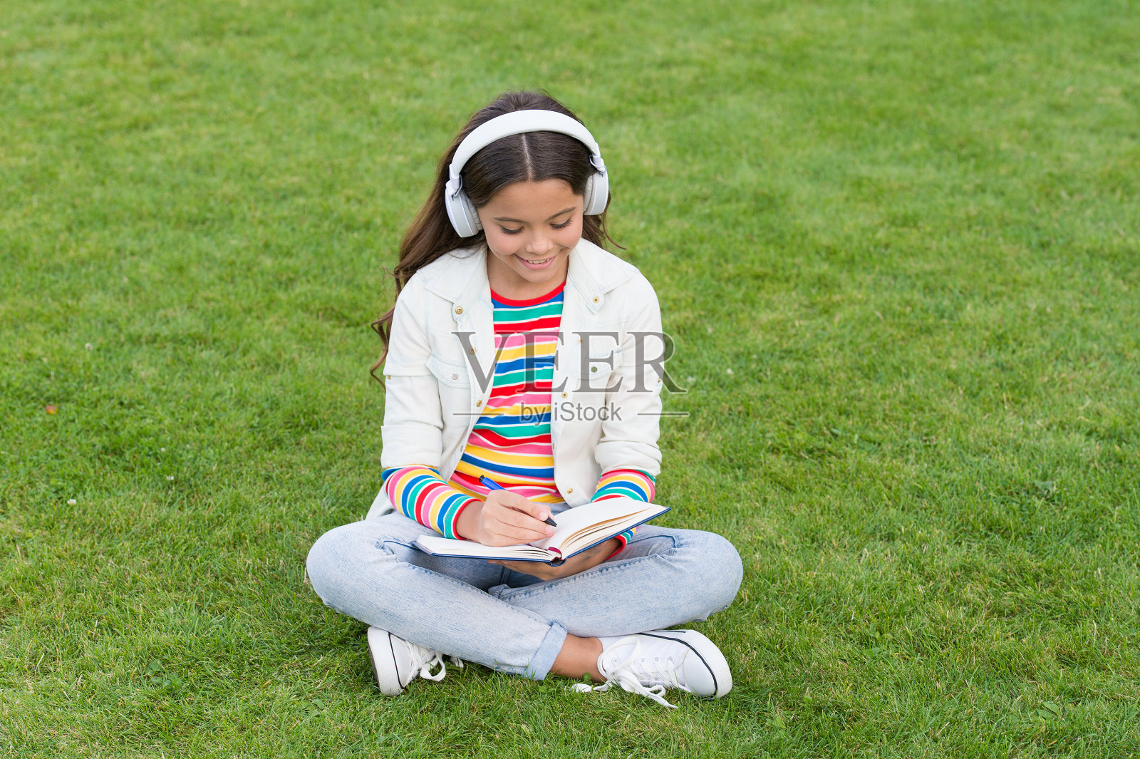 在线学习。教育播客。让它发生。在户外听音乐。小女孩坐在草地上享受音乐。愉快的时间。儿童耳机听音乐。酷女孩戴着耳机听音乐照片摄影图片